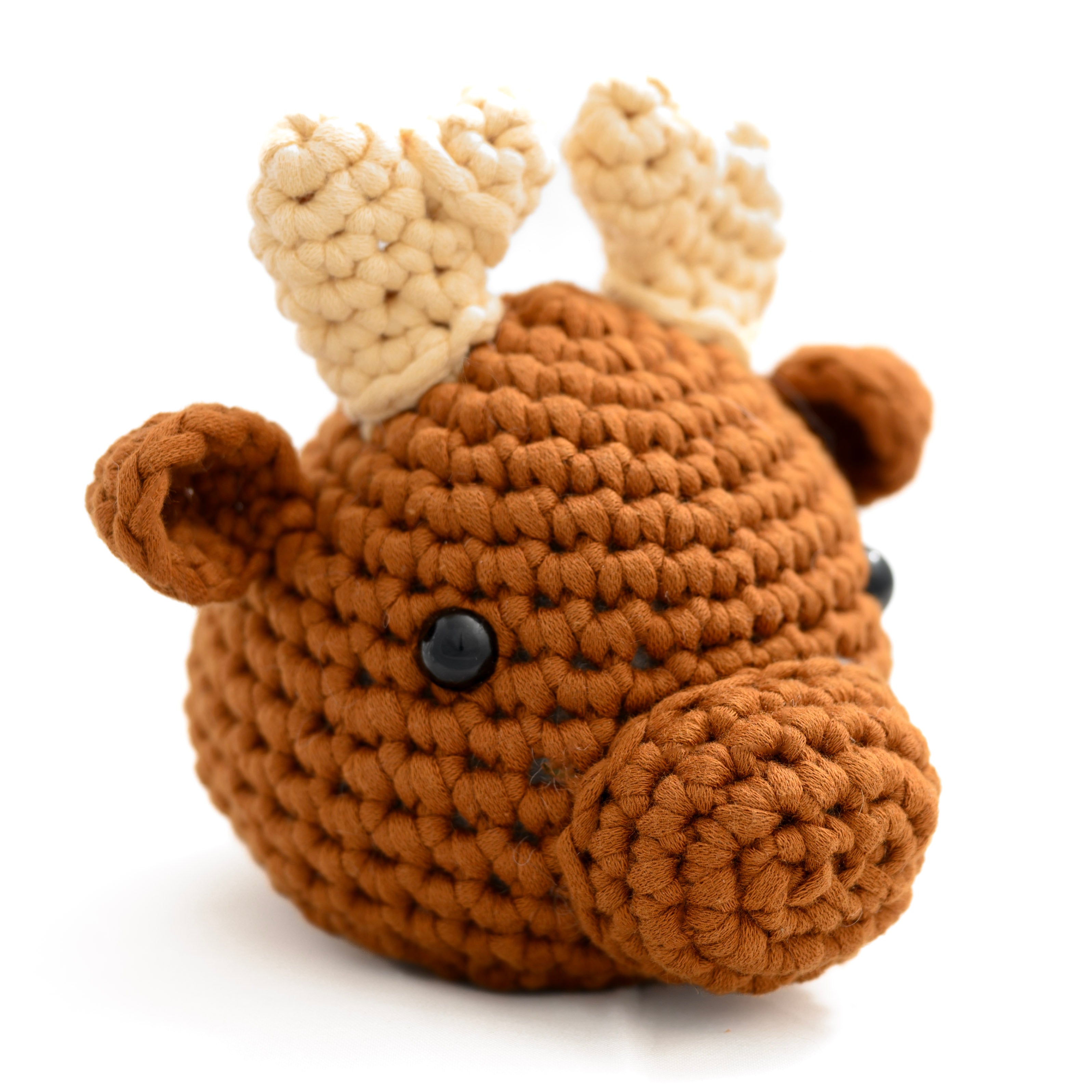 A crocheted plush toy shaped like a moose head, featuring a warm brown body, cream-colored antlers, black bead eyes, and a soft textured surface on a clean white background.